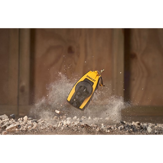 STANLEY STHT0-47147 chalk line in yellow and black, shown kicking up dust on rocky ground, action shot.