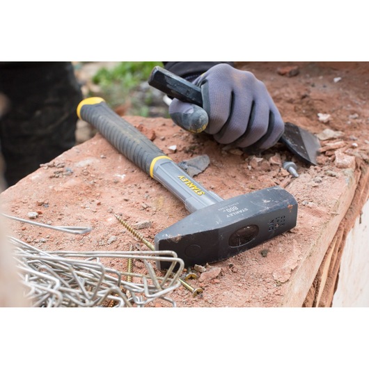 STANLEY STHT0-51909 sledge hammer with black handle on a workbench near metal fasteners and gloved hand.