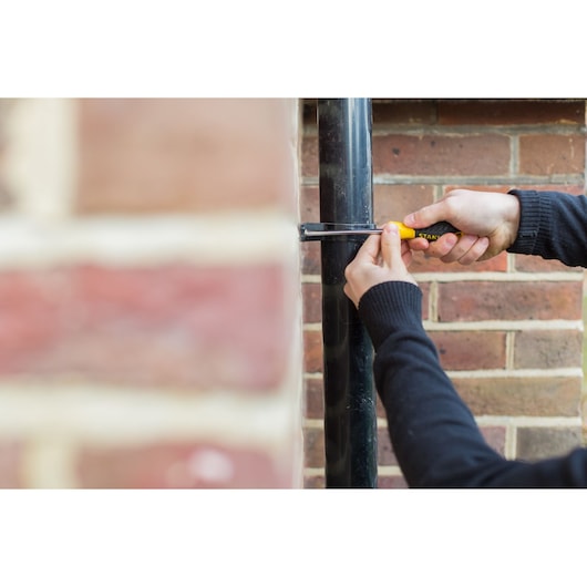 Photo of STANLEY STHT0-60274 screwdriver being used on black pipe against brick wall.