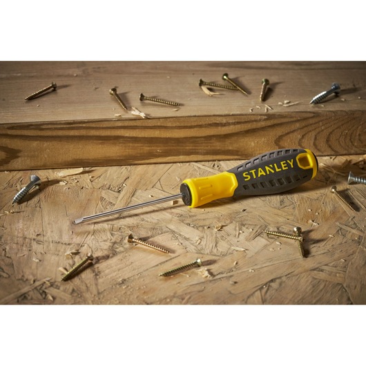 STANLEY STHT0-60358 flathead screwdriver with yellow and black handle on wooden surface with scattered screws.
