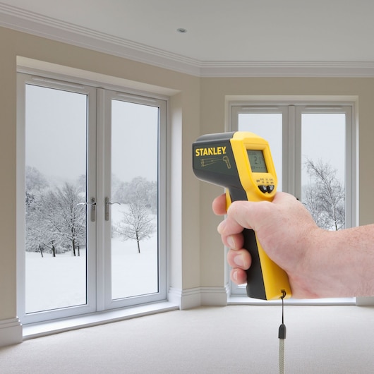 Stanley STHT0-77365 infrared thermometer held in hand, measuring window temperature indoors.