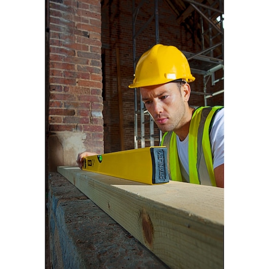 Photo of STANLEY STHT1-43102 spirit level in use on wooden beam at construction site.