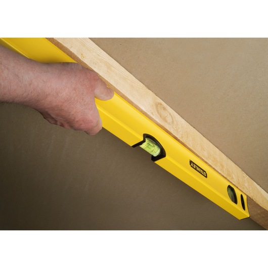 STANLEY STHT1-43103 yellow spirit level held against wood, side view, used for precise leveling.