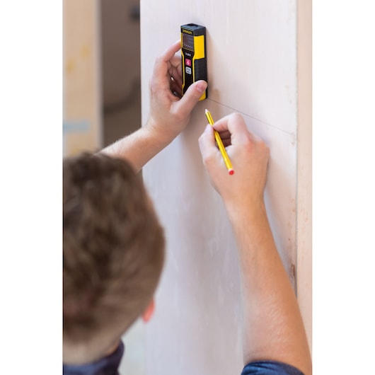 STANLEY STHT1-77032 laser measurer held against wall, person marking line with pencil.