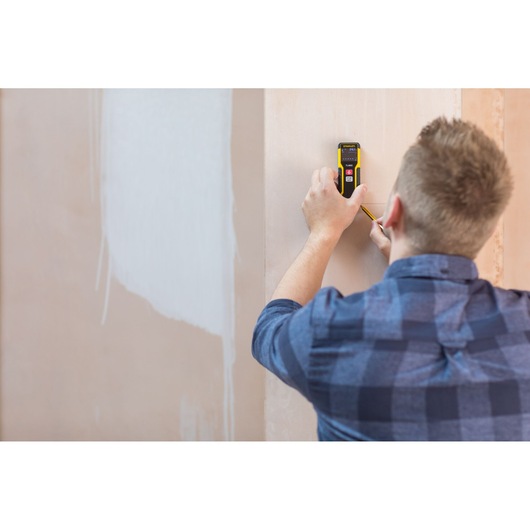 STANLEY STHT1-77032 digital wall scanner held against wall, person marking spot, photography product in use.
