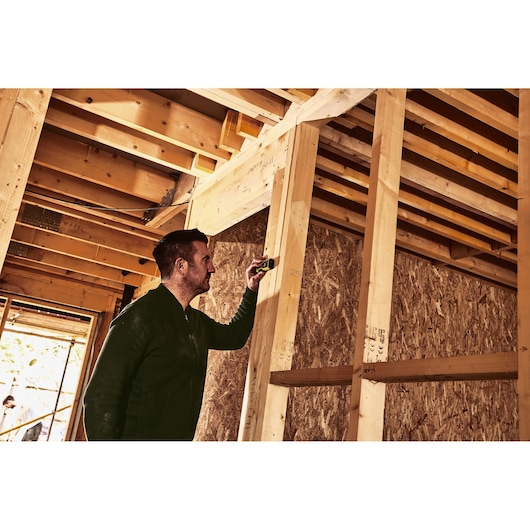 Photo of STANLEY STHT1-77409 laser distance measurer used by a person on a wood framing construction site.