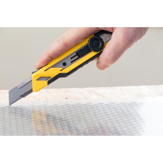 Photo of STANLEY STHT10268-1 utility knife cutting material, yellow and black handle, side angle.