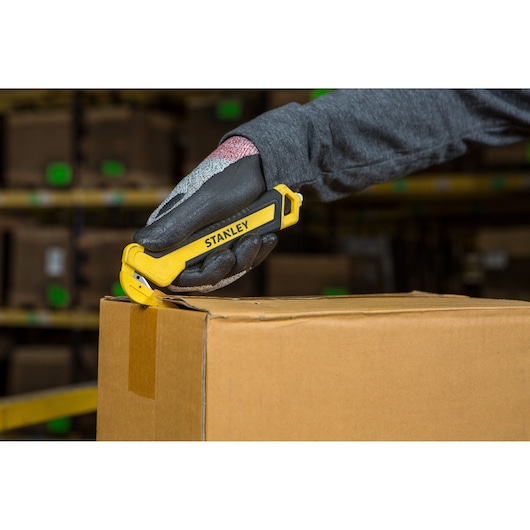 STANLEY STHT10356-0 safety utility knife cutting a cardboard box, handheld, warehouse background.