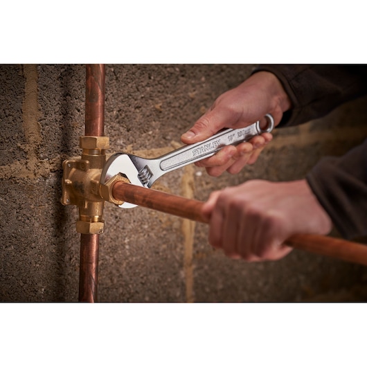 Photo of STANLEY STHT13122-0 adjustable wrench being used on copper plumbing pipe against masonry wall.