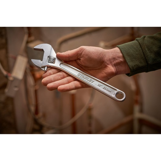 Photo of a hand holding a STANLEY STHT13122-0 adjustable wrench, silver, 250mm, in a workshop setting.