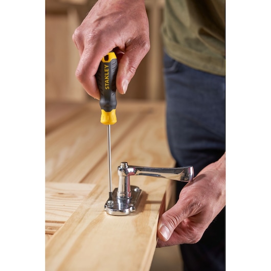 STANLEY STHT16195-0 screwdriver with black and yellow handle used to fasten a hinge on a wooden surface.