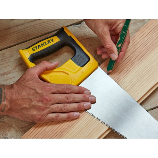 Stanley STHT20350-1 hand saw with yellow and black handle on wood, person marking with pencil.