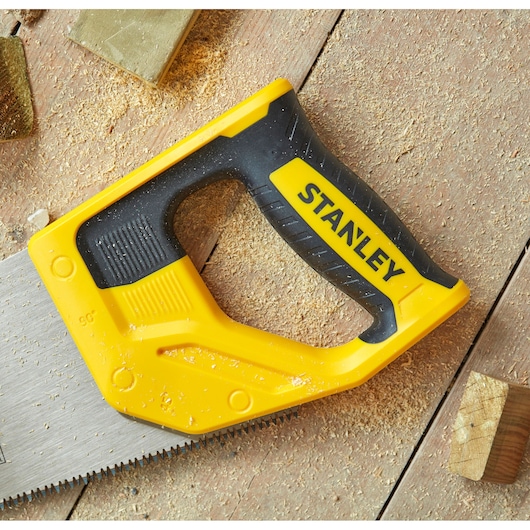 STANLEY STHT20350-1 hand saw with yellow and black handle, photography of saw on wood surface with sawdust.
