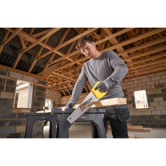 STANLEY STHT20366-1 hand saw cutting wood on saw horse, indoor construction site.