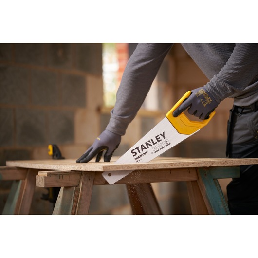 Photo of STANLEY STHT20366-1 hand saw with yellow handle cutting wood, used by a person wearing gloves.