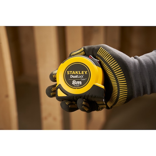 Photo of STANLEY STHT36804-0 tape measure, yellow and black, 8m length, held by gloved hand, product category photography.
