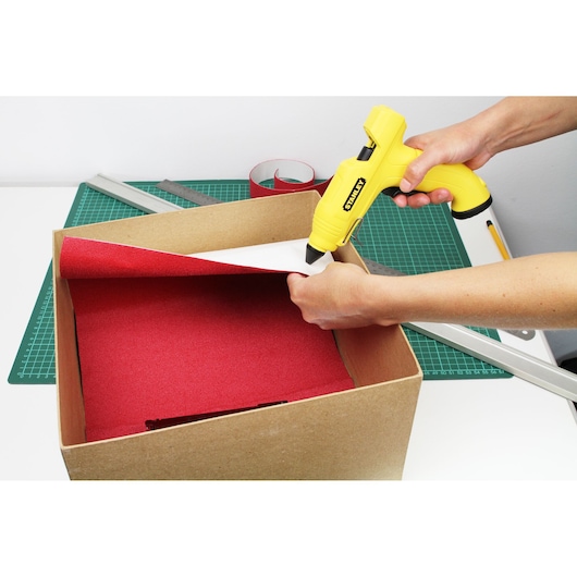 STANLEY STHT6-70416 yellow glue gun used for crafting with red paper in a cardboard box, side angle.
