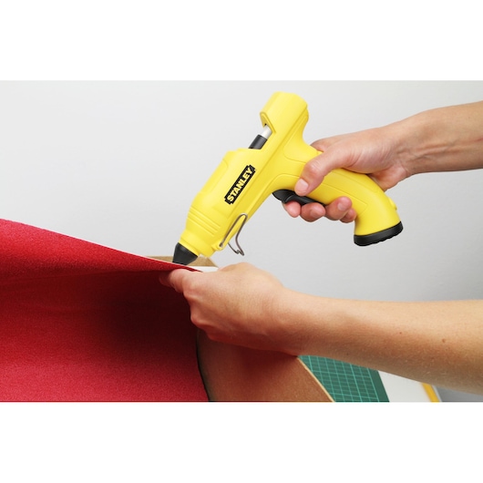 Stanley STHT6-70416 yellow glue gun held applying adhesive to red fabric, close-up photography.