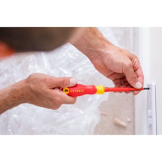 STANLEY STHT60031-0 screwdriver with red and yellow handle used on a wall switch, close-up photo.
