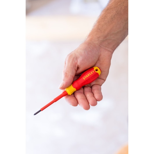 Photo of STANLEY STHT60031-0 insulated screwdriver with red and yellow handle, held in a hand, side view.