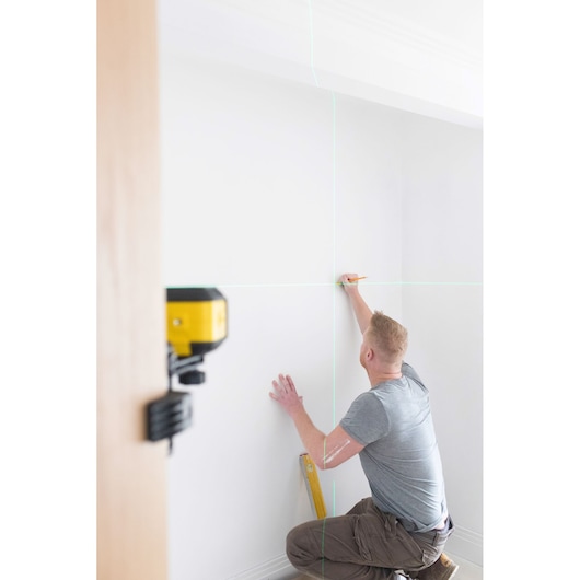 STANLEY STHT77499-1 laser level projecting lines on wall, person marking measurements, interior use.