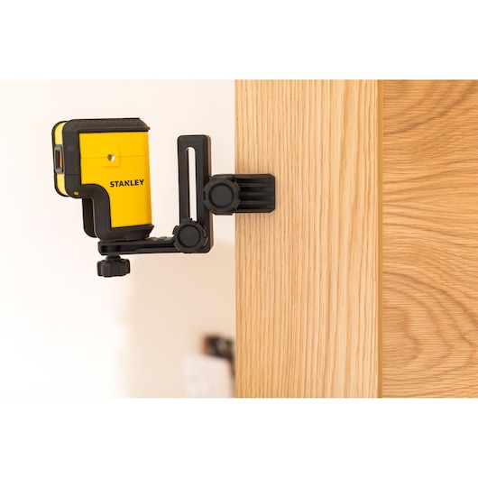 STANLEY STHT77503-1 yellow laser level mounted on black clamp attached to a wooden surface.