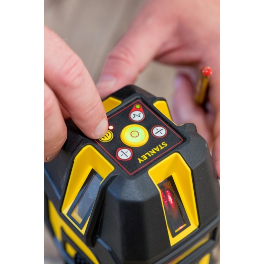 STANLEY STHT77514-1 laser level top control panel close-up with hand pushing yellow button.