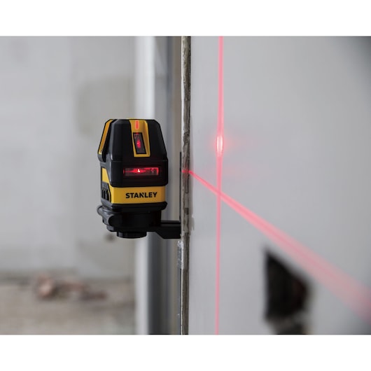 STANLEY STHT77514-1 self-leveling cross line laser emitting red laser lines on a wall in a construction setting.