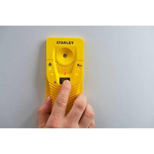 STANLEY STHT77587-0 yellow stud finder held against wall, front angle view, lights illuminated.