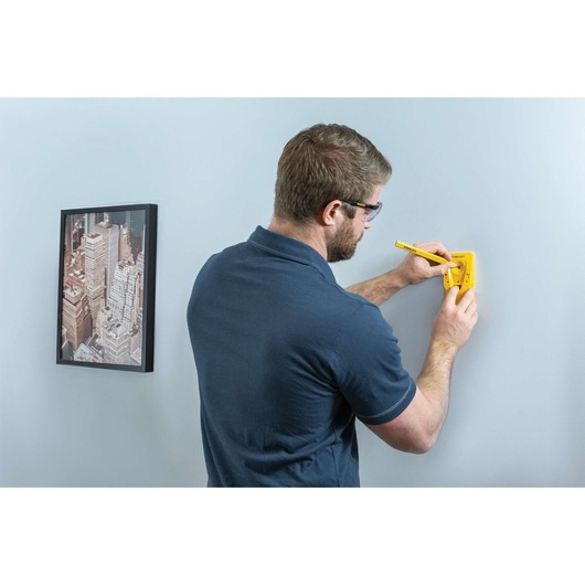 Photo of a person using a STANLEY STHT77587 stud finder on a wall, marking position with a pencil.