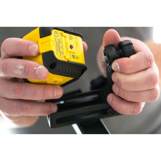 Photo of hands holding a STANLEY STHT77648-1 yellow laser level and mounting bracket.