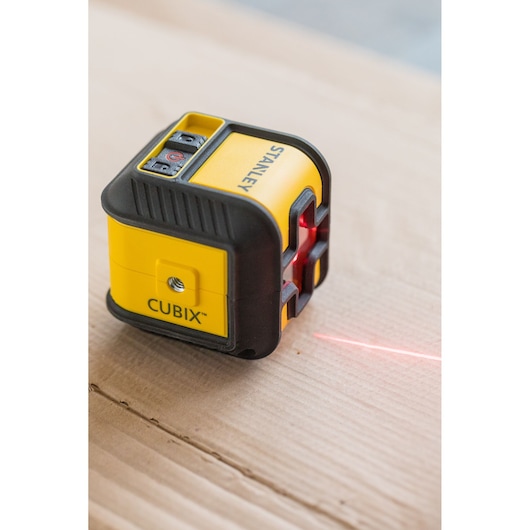STANLEY STHT77648-1 CUBIX laser level, compact yellow and black tool, projecting red laser line on wood surface.