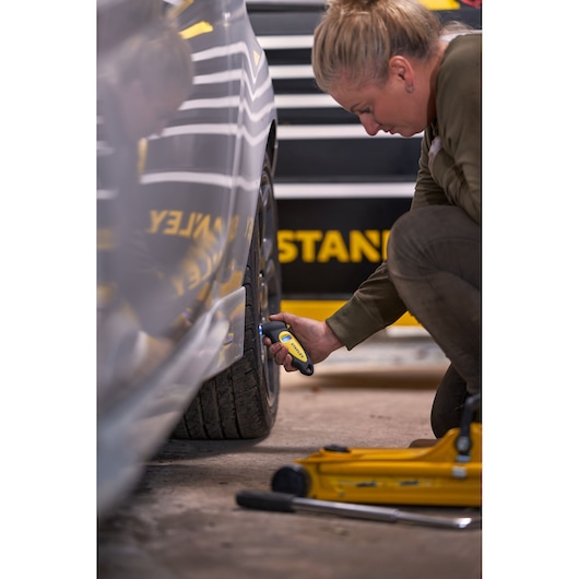 Photo of STANLEY STHT80874-0 tire pressure gauge used on car tire in garage setting.
