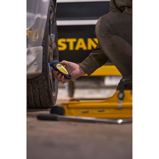 Photo of STANLEY STHT80874-0 digital tire gauge in use on a car wheel near automotive tools.