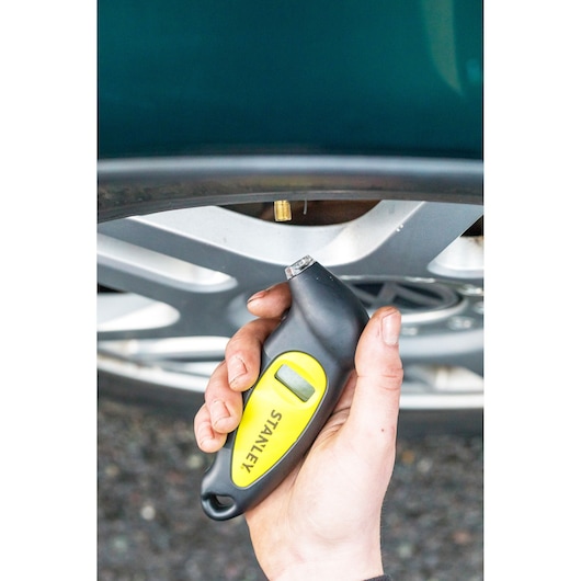 STANLEY STHT80874-0 digital tire pressure gauge held near a car wheel valve.