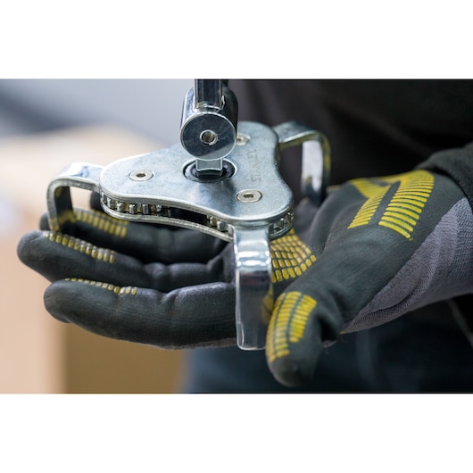 Photo of STANLEY STHT80880-0 adjustable oil filter wrench held in gloved hands, close-up view.