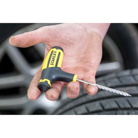Stanley STHT80891-0 T-handle tire repair tool with spiral probe held in hand near a car tire.