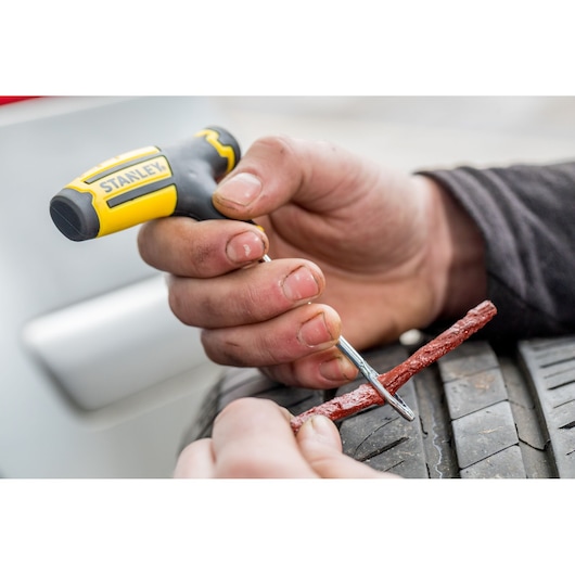 Stanley STHT80891-0 tire repair tool in use inserting plug into car tire.