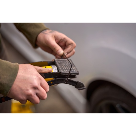 Photo of hands using STANLEY STHT80894-1 tool near a vehicle, focusing on detailed grip and metal part.