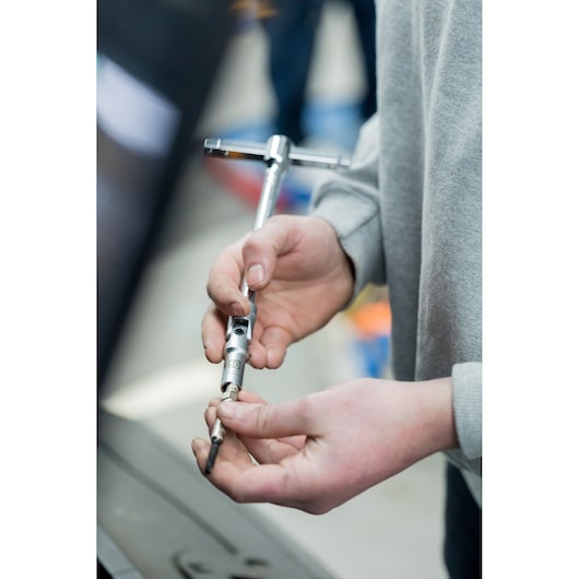Photo of hands using STANLEY STHT81016-0 ratchet tap wrench, close-up during workshop use.