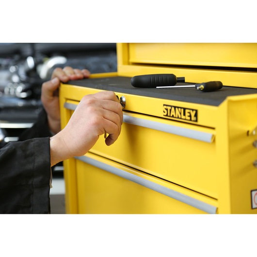 Photo of STANLEY STMT1-75063 yellow tool chest drawer being locked by hand, tools on top.