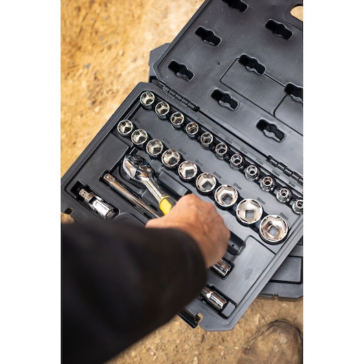 STANLEY STMT82830-1 socket set with ratchet, sockets, and accessories in black case, hand reaching for tool.