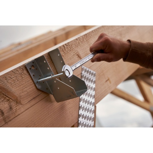 STANLEY STMT82843-0 combination wrench tightening bolt on wooden beam, close-up in construction setting.