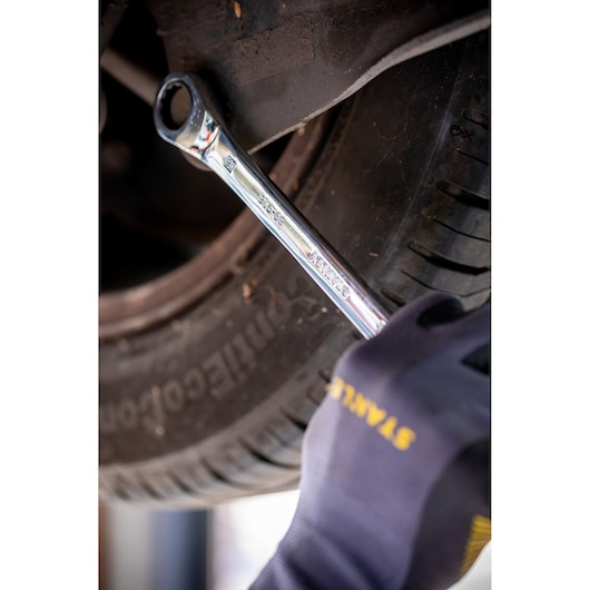 STANLEY STMT82847-0 combination wrench used on a car wheel, gloved hand visible.