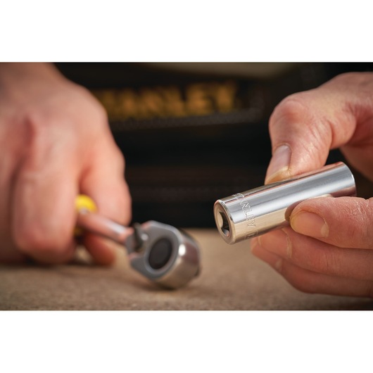 STANLEY STMT86098-0 socket held by hand, close-up with ratchet tool in background.