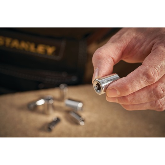 STANLEY STMT86109-0 chrome socket held in hand with other sockets on work surface, close-up photography.