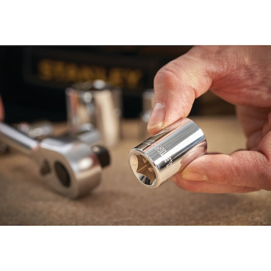 STANLEY STMT86520-0 chrome socket held by hand, with ratchet wrench and other sockets visible in background.