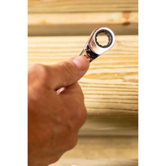 STANLEY STMT89912-0 ratcheting wrench held in hand, close-up view against wooden background.