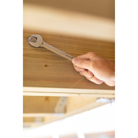 Photo of STANLEY STMT89916-0 wrench being used on a bolt in wooden beam, close-up hand holding tool.
