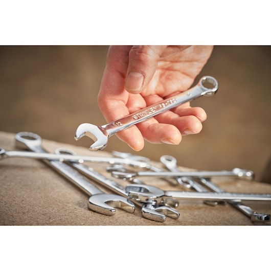 Photo of hand holding STANLEY STMT95789-0 combination wrench with other wrenches on work surface.
